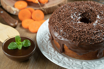 Brazilian carrot cake with chocolate frosting on wooden table with carrots in the background