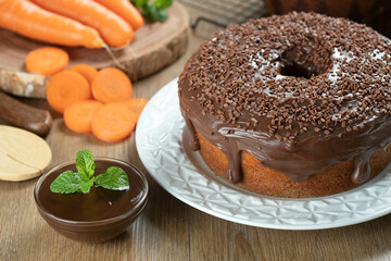 Brazilian carrot cake with chocolate frosting on wooden table with carrots in the background