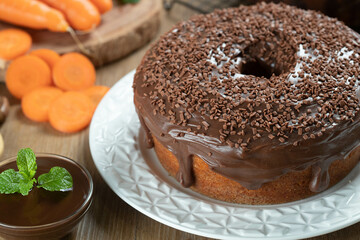 Brazilian carrot cake with chocolate frosting on wooden table with carrots in the background