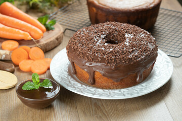 Brazilian carrot cake with chocolate frosting on wooden table with carrots in the background