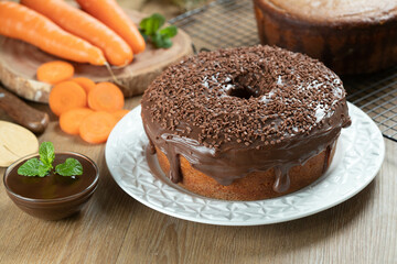 Brazilian carrot cake with chocolate frosting on wooden table with carrots in the background