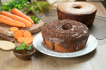 Brazilian carrot cake with chocolate frosting on wooden table with carrots in the background
