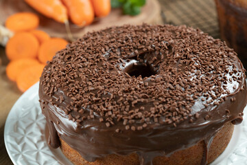 Brazilian carrot cake with chocolate frosting on wooden table with carrots in the background