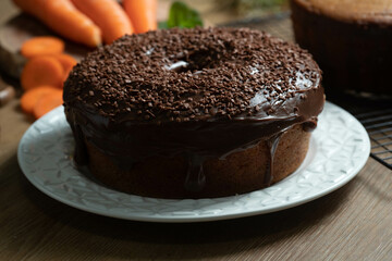 Brazilian carrot cake with chocolate frosting on wooden table with carrots in the background