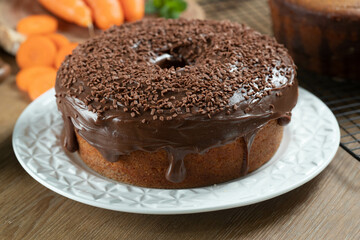 Brazilian carrot cake with chocolate frosting on wooden table with carrots in the background