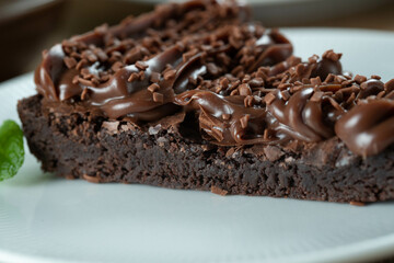 Piece of Chocolate Brownie Slice with Strawberry and Chocolate Icing. Wooden table with mint and chocolate chips in the background