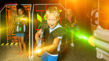 Emotional teen boy with laser pistol playing laser tag with friends on dark labyrinth. High quality photo