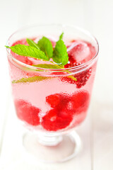Raspberry cocktail.Summer drink.raspberry pink drink.Ice cubes with raspberries in a glass with mineral water, berries and raspberry leaves on a white wooden table. 