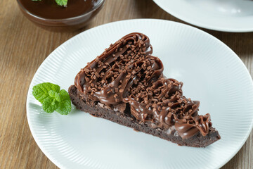 Piece of Chocolate Brownie Slice with Strawberry and Chocolate Icing. Wooden table with mint and chocolate chips in the background. Top view.