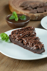 Piece of Chocolate Brownie Slice with Strawberry and Chocolate Icing. Wooden table with mint and chocolate chips in the background