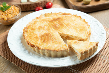 Chicken pie with cottage cheese, tomatoes, onion and olives on wooden table and white plate.