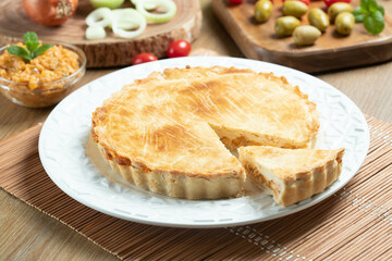Chicken pie with cottage cheese, tomatoes, onion and olives on wooden table and white plate.