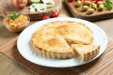 Chicken pie with cottage cheese, tomatoes, onion and olives on wooden table and white plate.
