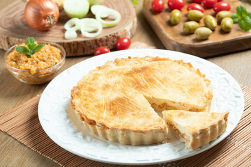 Chicken pie with cottage cheese, tomatoes, onion and olives on wooden table and white plate.
