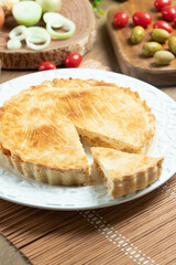 Chicken pie with cottage cheese, tomatoes, onion and olives on wooden table and white plate.