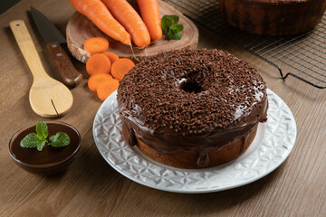 Brazilian carrot cake with chocolate frosting on wooden table with carrots in the background