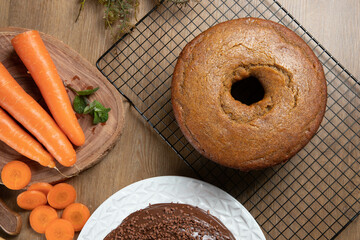 Brazilian carrot cake with chocolate frosting on wooden table with carrots in the background. Top view.