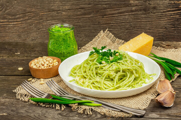 Spaghetti pasta with pesto sauce and fresh ramson leaves. Cutlery, parmesan, pine nuts. Rustic style