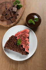 Piece of Chocolate Brownie Slice with Strawberry and Chocolate Icing. Wooden table with mint and chocolate chips in the background. Top view