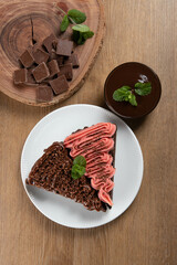 Piece of Chocolate Brownie Slice with Strawberry and Chocolate Icing. Wooden table with mint and chocolate chips in the background. Top view