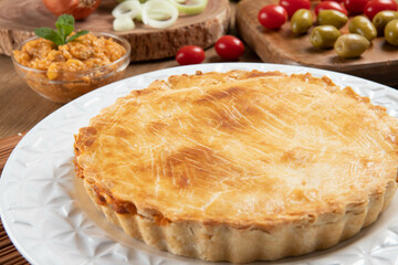 Chicken pie with cottage cheese, tomatoes, onion and olives on wooden table and white plate