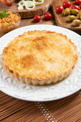 Chicken pie with cottage cheese, tomatoes, onion and olives on wooden table and white plate