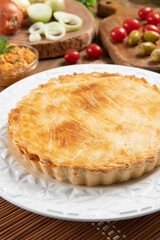 Chicken pie with cottage cheese, tomatoes, onion and olives on wooden table and white plate