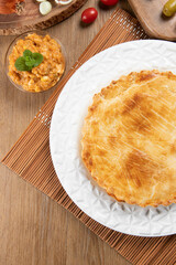 Chicken pie with cottage cheese, tomatoes, onion and olives on wooden table and white plate. Top view