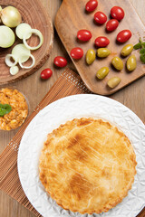 Chicken pie with cottage cheese, tomatoes, onion and olives on wooden table and white plate. Top view