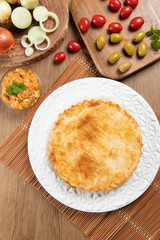 Chicken pie with cottage cheese, tomatoes, onion and olives on wooden table and white plate. Top view
