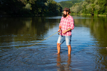 Fototapeta na wymiar Young bearded man fishing at a lake or river. Flyfishing.