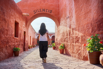 Turista latina caminando de espaldas entrando al arco Silencio del monasterio Santa Catalina en Arequipa - obrazy, fototapety, plakaty