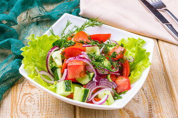 Vegetable salad with tomatoes and cucumbers and red onion on wooden table