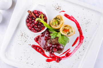 Venison steak with lingonberry sauce on a white plate top view