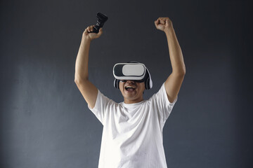 Enthusiastic asian man using VR and console is celebrating victory, winning games or competition, achieve goal, dark grey background