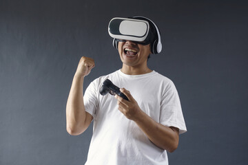 Enthusiastic asian man using VR and console is celebrating victory, smiling saying yes, winning...