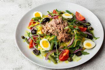 French salad Nicoise with tuna, egg, green beans, tomatoes, olives, lettuce, onions and anchovies on a white background. Healthy food