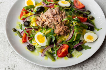 French salad Nicoise with tuna, egg, green beans, tomatoes, olives, lettuce, onions and anchovies on a white background. Healthy food