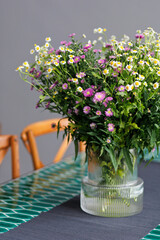 White and purple daisy bouquet in glass jar on table close up. Selective focus image.