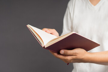 Close-up of man in white casual holding a book while standing on a gray background