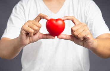 Close-up of hand holding a red heart shape while standing on a gray background