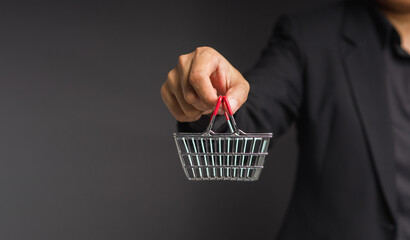 Close-up of hand holding an empty mini shopping cart over a gray background.