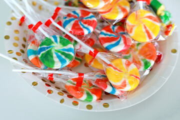 Fototapeta premium Colourful candies, lollypops in transparent plastic wrapping on a plate.