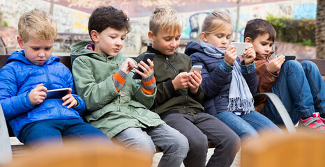 Group of preteen children sitting on bench outdoors, addicted in their phones.