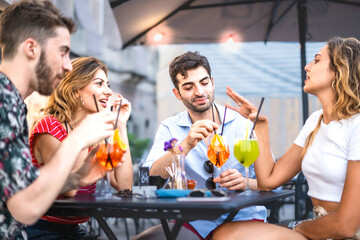 Four trendy young people get together carefree sitting and bonding at outdoors bar restaurant -...