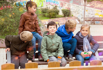 Group of cheerful children chatting while relaxing on bench on playground..