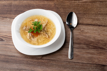 Tasty chicken soup bouillon with noodles, chicken meat, dill and parsley in a white bowl. Isolated on wooden background. Healthy meal menu.