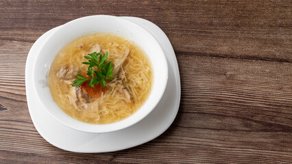 Tasty chicken soup bouillon with noodles, chicken meat, dill and parsley in a white bowl. Isolated on wooden background. Healthy meal menu.