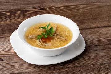 Tasty chicken soup bouillon with noodles, chicken meat, dill and parsley in a white bowl. Isolated on wooden background. Healthy meal menu.