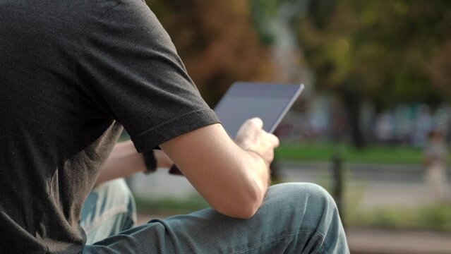 Back view of man wearing casual clothes, sitting on steps, using tablet. Close up of stylish male in big city connecting with people online, messaging and browsing Internet. 4k footage